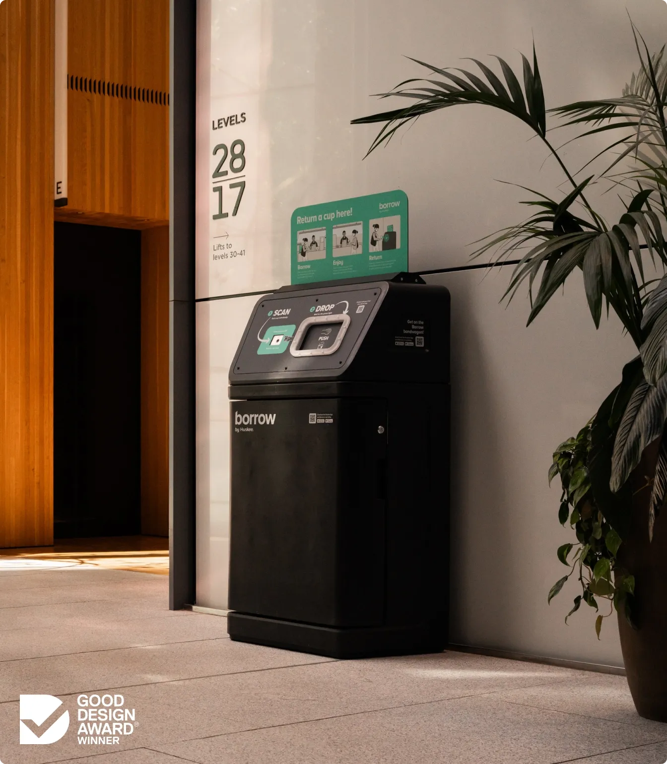 A Borrow bin beside the lifts in an office lobby, with the Good Design Award winner mark