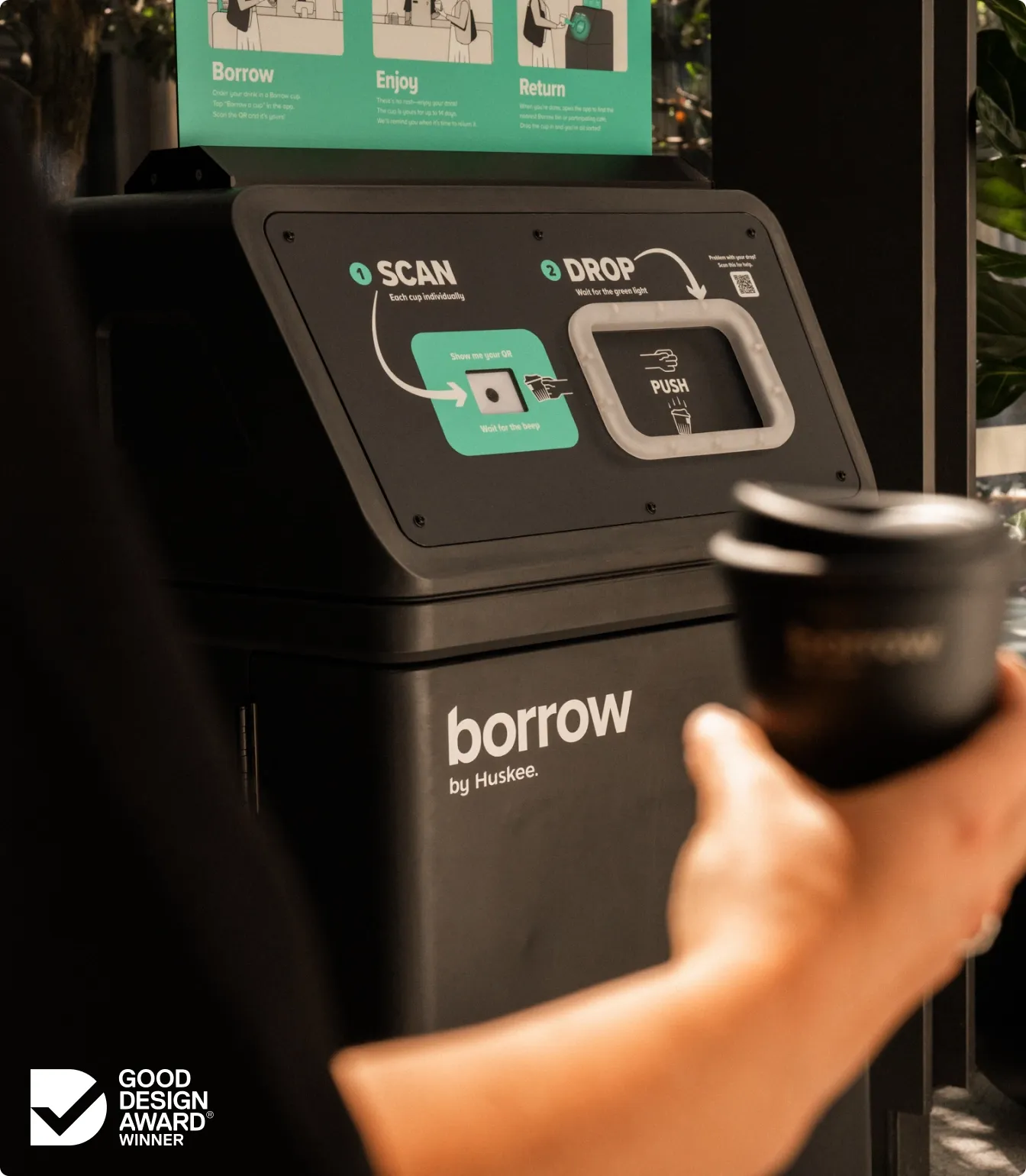 A hand holding a Borrow cup out towards the bin's scan pad