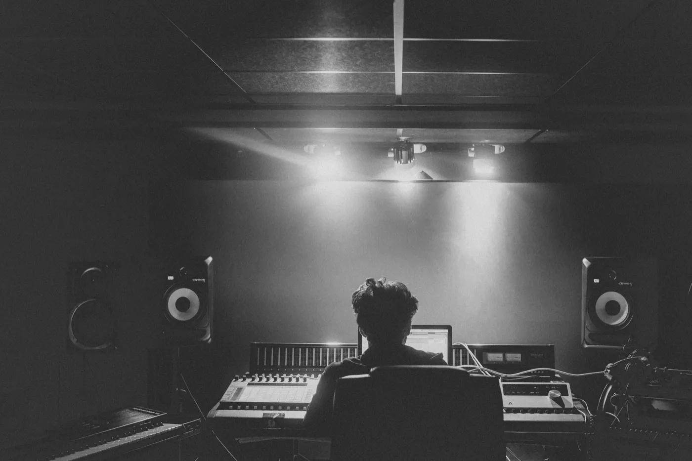 A studio engineer at a mixing desk in a darkened control room, shot in black and white