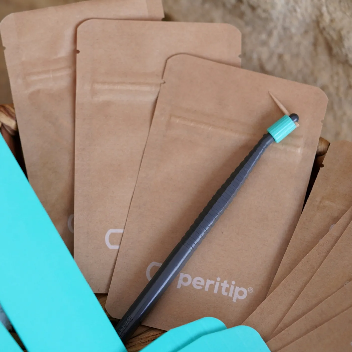 A stack of kraft Peritip sachets with a teal applicator resting across them